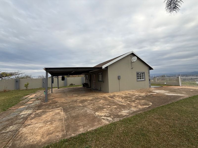 Rear view of the property featuring a large concrete driveway, a covered carport, and secure perimeter walling.