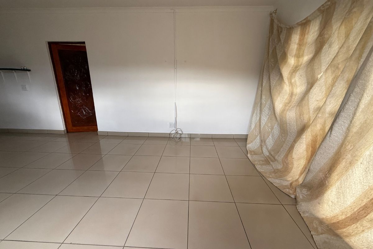 An empty living area featuring neutral ceramic floor tiles, a solid wooden door, and white walls with surface-mounted electrical wiring.