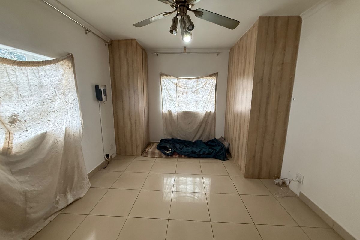 A bedroom featuring tiled flooring, built-in wooden cupboards, and a ceiling fan, offering a functional space ready for personalization.