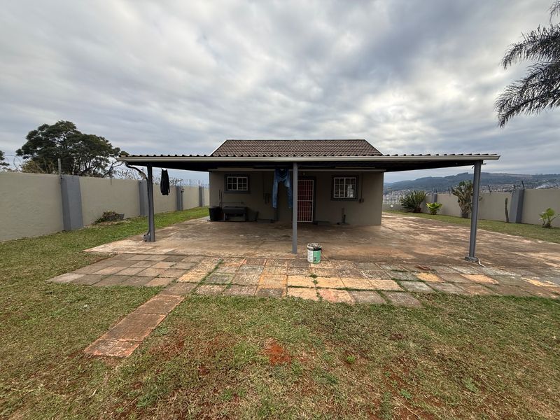 Rear view of the property featuring a covered patio area, perimeter walling, and a paved outdoor space with potential for landscaping improvements.