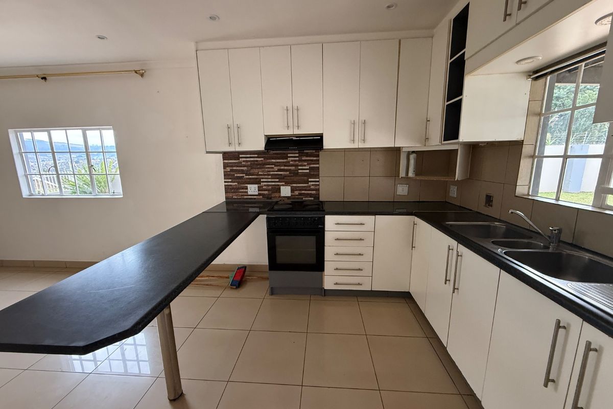 A functional kitchen featuring white cabinetry, black stone countertops, a breakfast bar, and a tiled backsplash with a built-in stove and double sink.