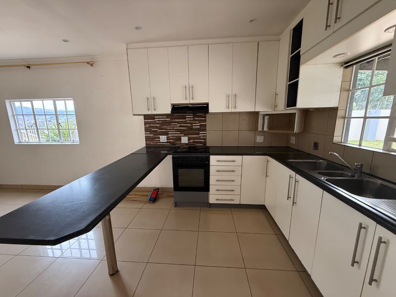 A functional kitchen featuring white cabinetry, black stone countertops, a breakfast bar, and a tiled backsplash with a built-in stove and double sink.