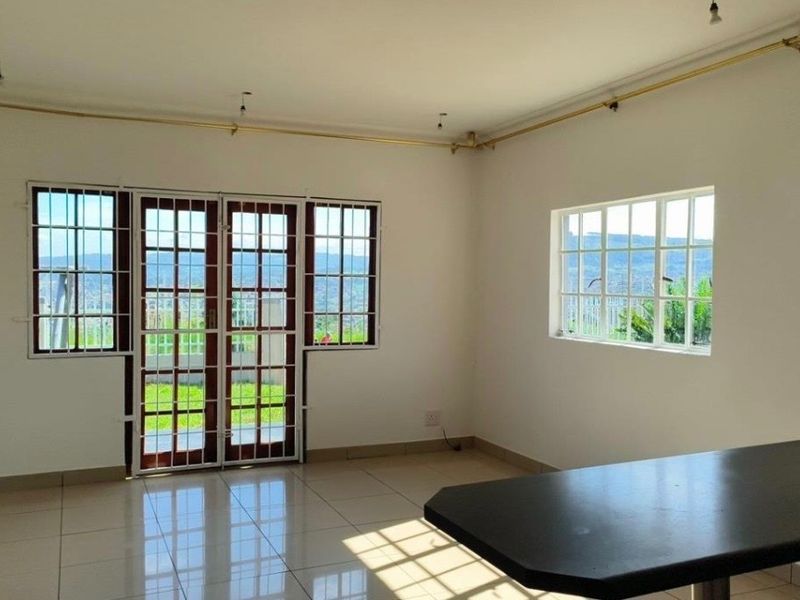 An open-plan living area featuring tiled flooring, a breakfast bar, and large windows with security bars, offering natural light and views.