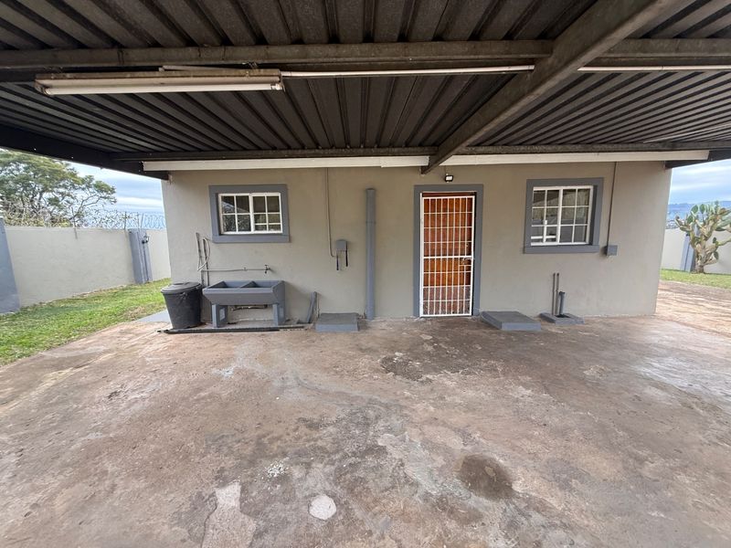 Rear exterior area featuring a covered concrete patio, laundry sink, and secure access door, set against a perimeter wall.