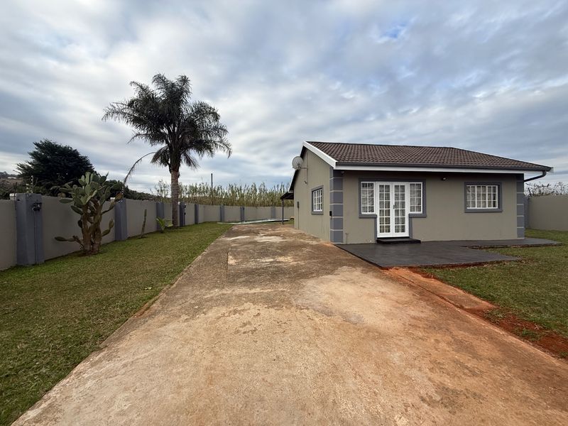 Rear view of a single-story house featuring a concrete driveway, perimeter wall with electric fencing, and a tiled roof.