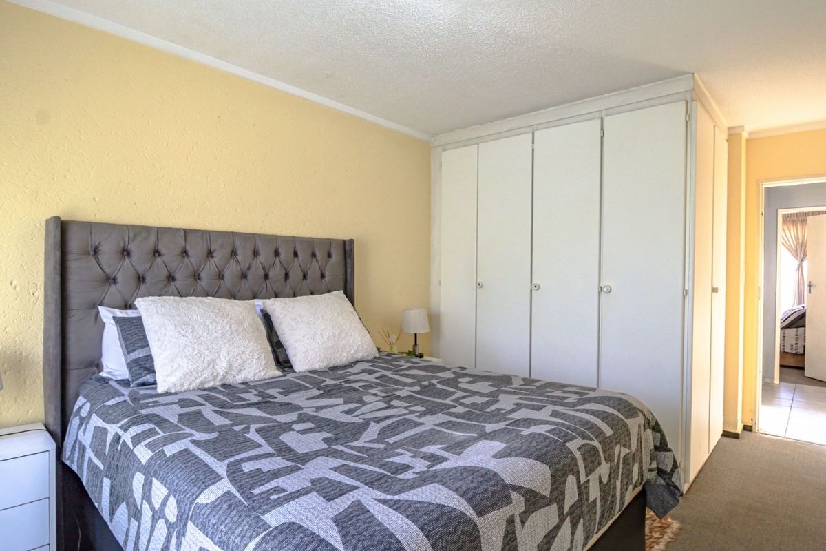 A bedroom featuring built-in cupboards and carpeted flooring, with a view into the adjacent hallway.