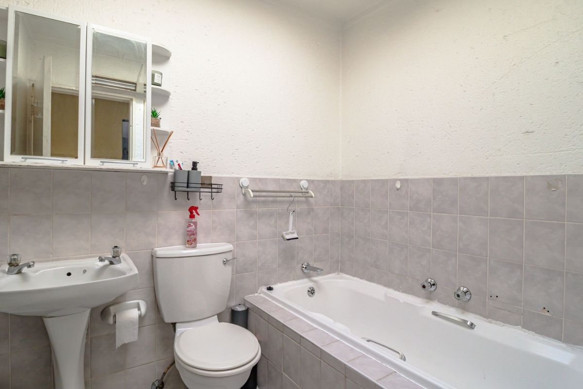 A functional bathroom featuring a pedestal basin, toilet, and built-in bathtub with tiled splashbacks and a wall-mounted medicine cabinet.