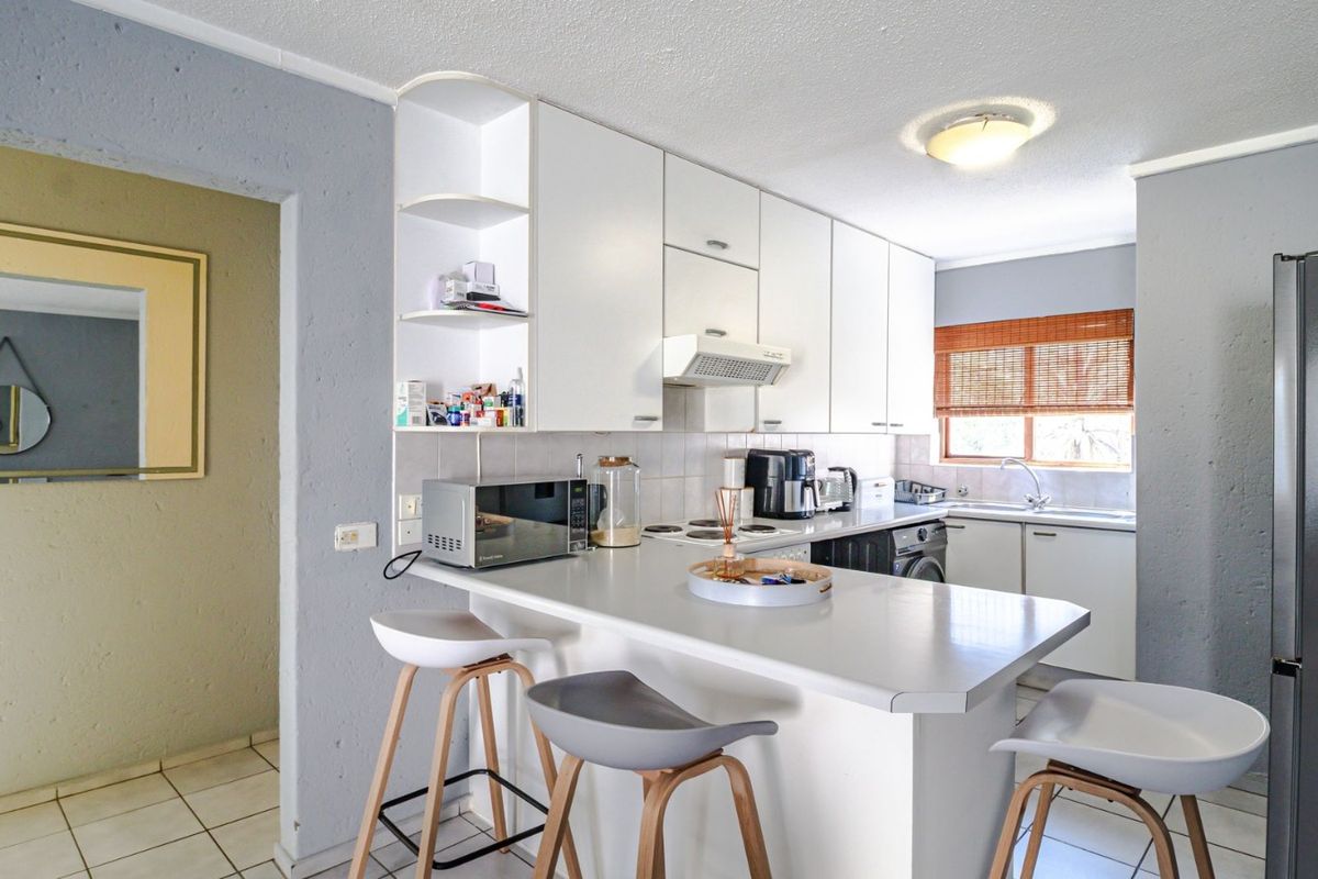 Functional kitchen featuring white cabinetry, a breakfast bar, tiled backsplash, and integrated cooking appliances, offering a practical layout for daily use.