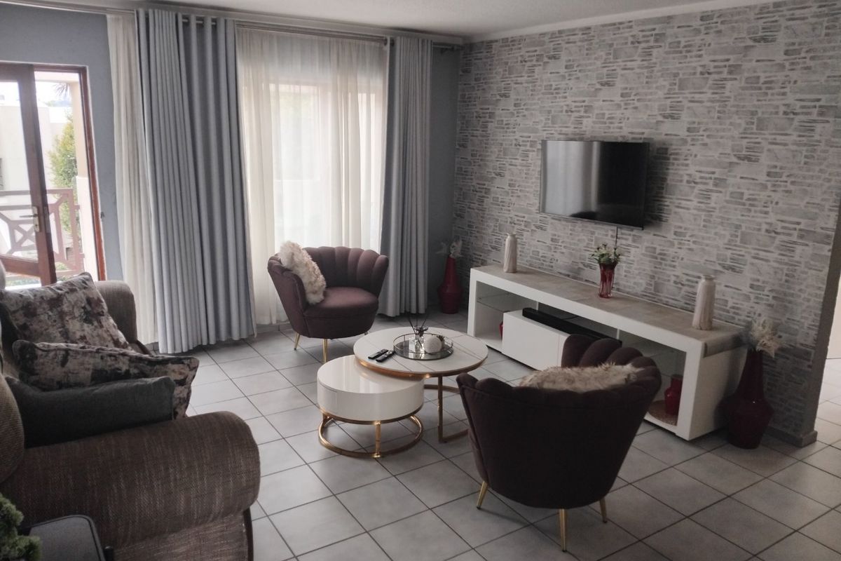 A well-maintained living room featuring tiled flooring, a textured feature wall, and direct access to an outdoor balcony through sliding glass doors.