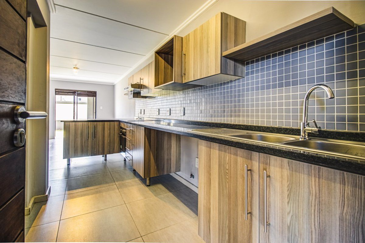 Modern kitchen featuring wood-look laminate cabinetry, granite countertops, mosaic tile backsplash, and integrated stainless steel sink with mixer tap.
