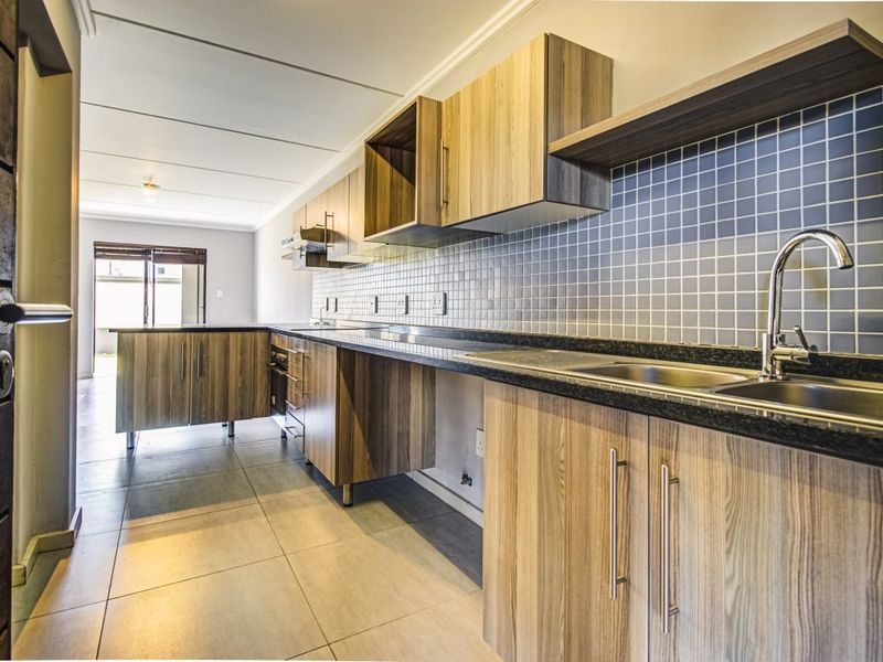 Modern kitchen featuring wood-look laminate cabinetry, granite countertops, mosaic tile backsplash, and integrated stainless steel sink with mixer tap.