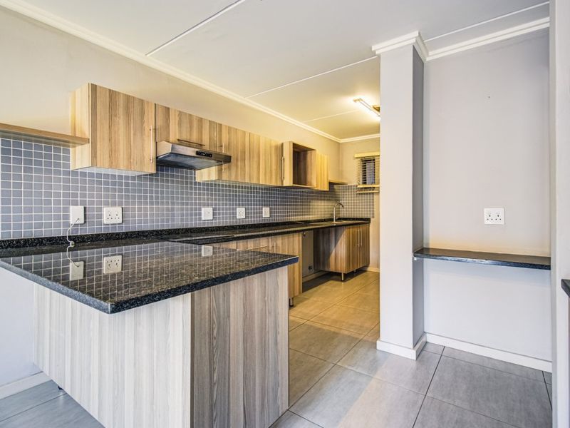 Modern kitchen featuring light wood-grain cabinetry, dark granite countertops, a tiled backsplash, and a functional breakfast bar layout.