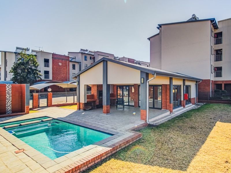 Communal pool area featuring a covered patio with built-in braai facilities, brick detailing, and paved surrounds within an apartment complex.