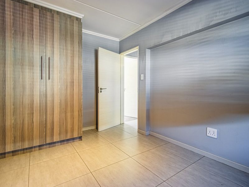 An empty bedroom featuring tiled flooring, built-in wooden cupboards, and neutral wall finishes, providing a blank canvas for personalization.