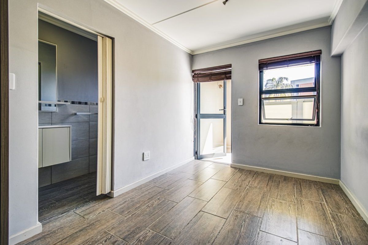 A bright, empty bedroom featuring wood-look tile flooring, an en-suite bathroom, and direct access to an outdoor area through a sliding door.