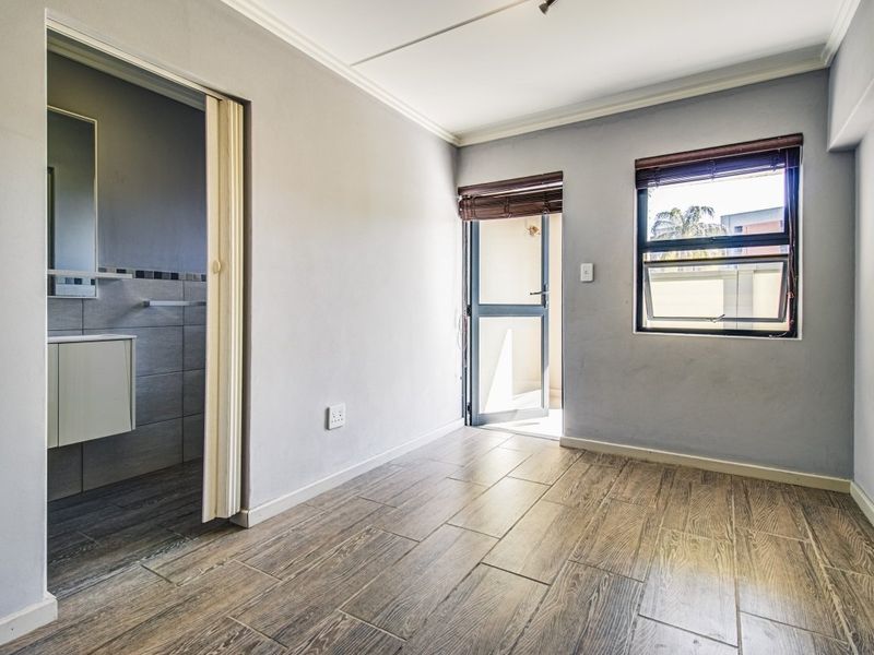 A bright, empty bedroom featuring wood-look tile flooring, an en-suite bathroom, and direct access to an outdoor area through a sliding door.
