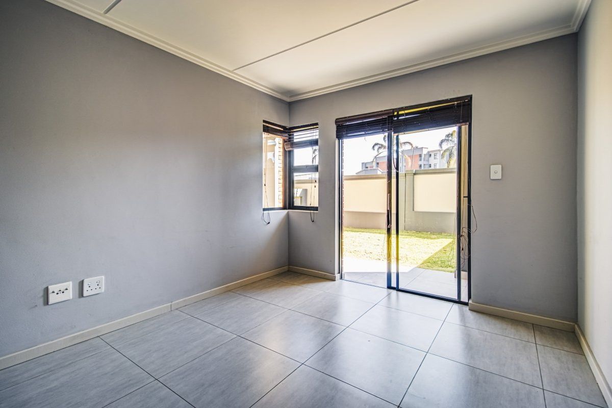An empty living room featuring neutral grey walls, large format floor tiles, and a sliding glass door providing access to the outdoor area.