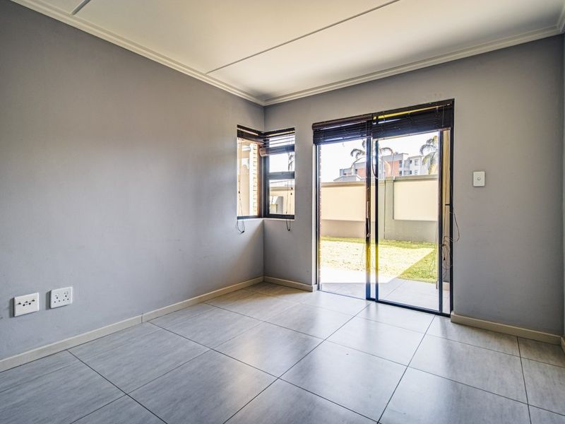 An empty living room featuring neutral grey walls, large format floor tiles, and a sliding glass door providing access to the outdoor area.