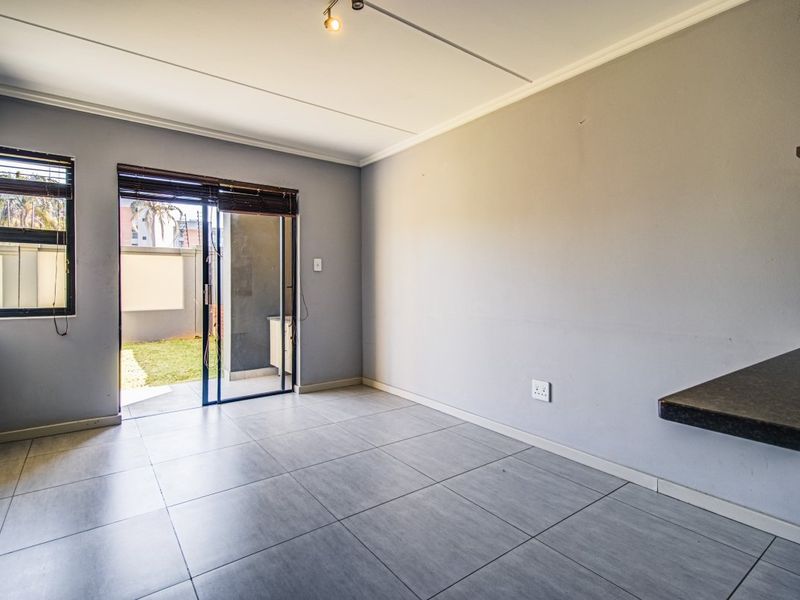 An empty open-plan living area featuring neutral grey tiled flooring, a breakfast counter, and a sliding glass door providing access to the outdoor space.