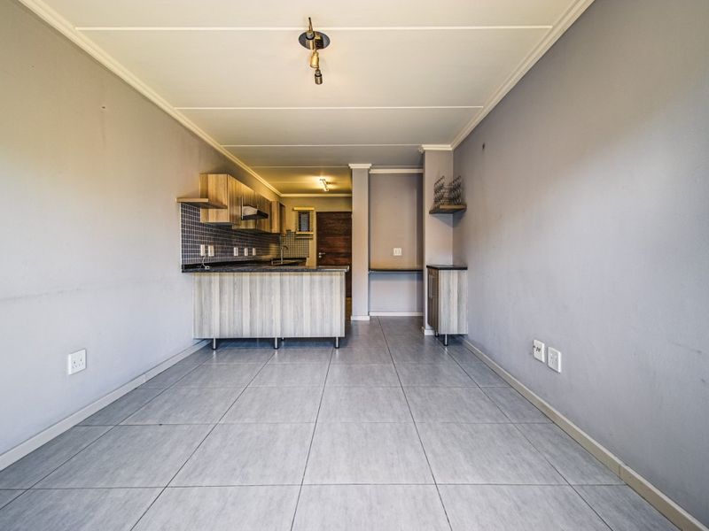 An open-plan living and kitchen area featuring tiled flooring, modern wood-finish cabinetry, and neutral wall tones, offering a versatile space for living and dining.