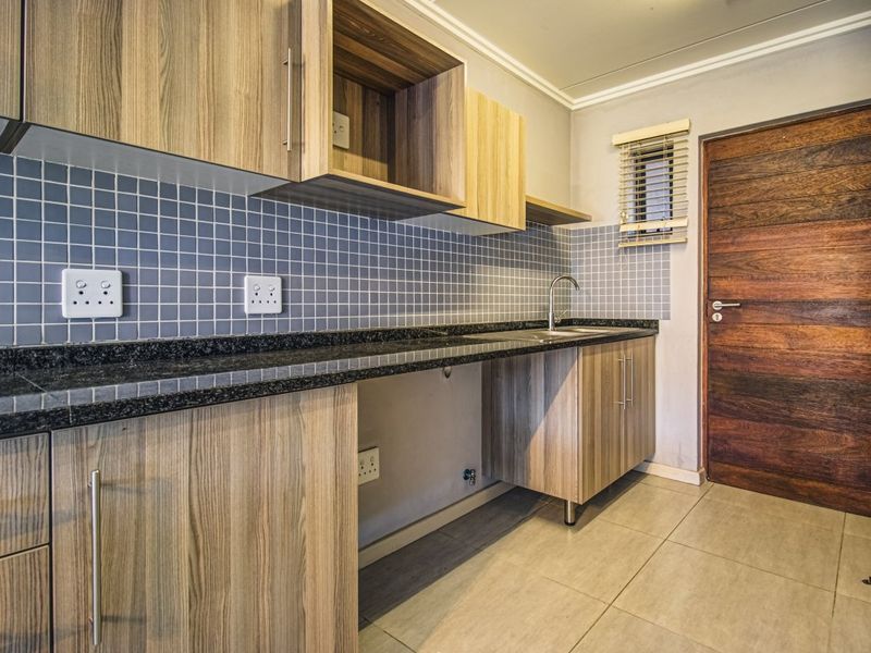 A clean, modern kitchen featuring wood-look cabinetry, granite countertops, a tiled backsplash, and neutral floor tiles, providing a functional and well-maintained workspace.