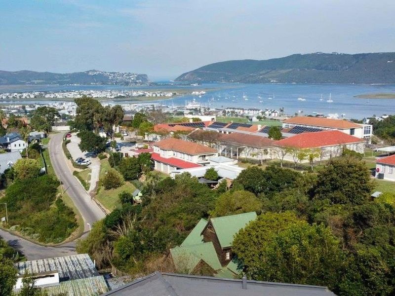 An elevated aerial view showcasing the surrounding neighbourhood, coastal landscape, and local infrastructure with prominent roof structures and solar installations.