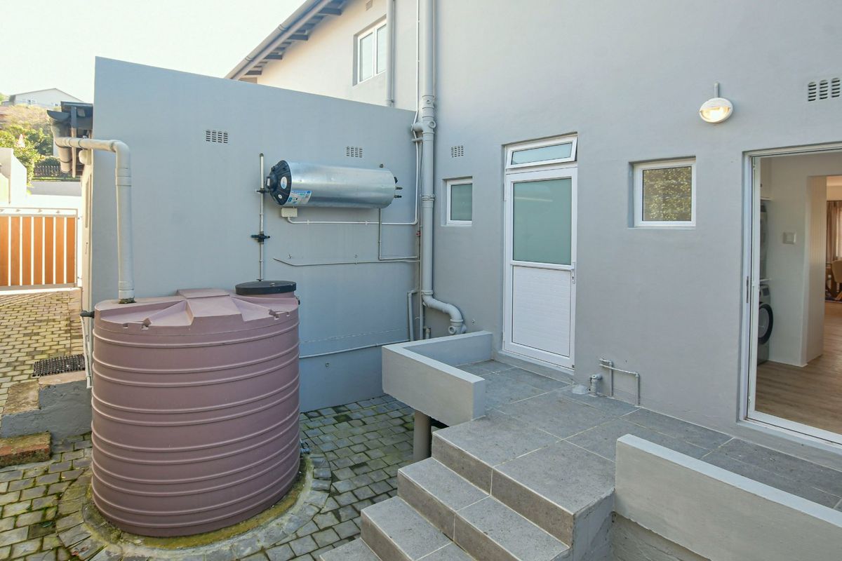Rear courtyard area featuring a water storage tank, wall-mounted electric geyser, paved flooring, and direct access to the interior living space.
