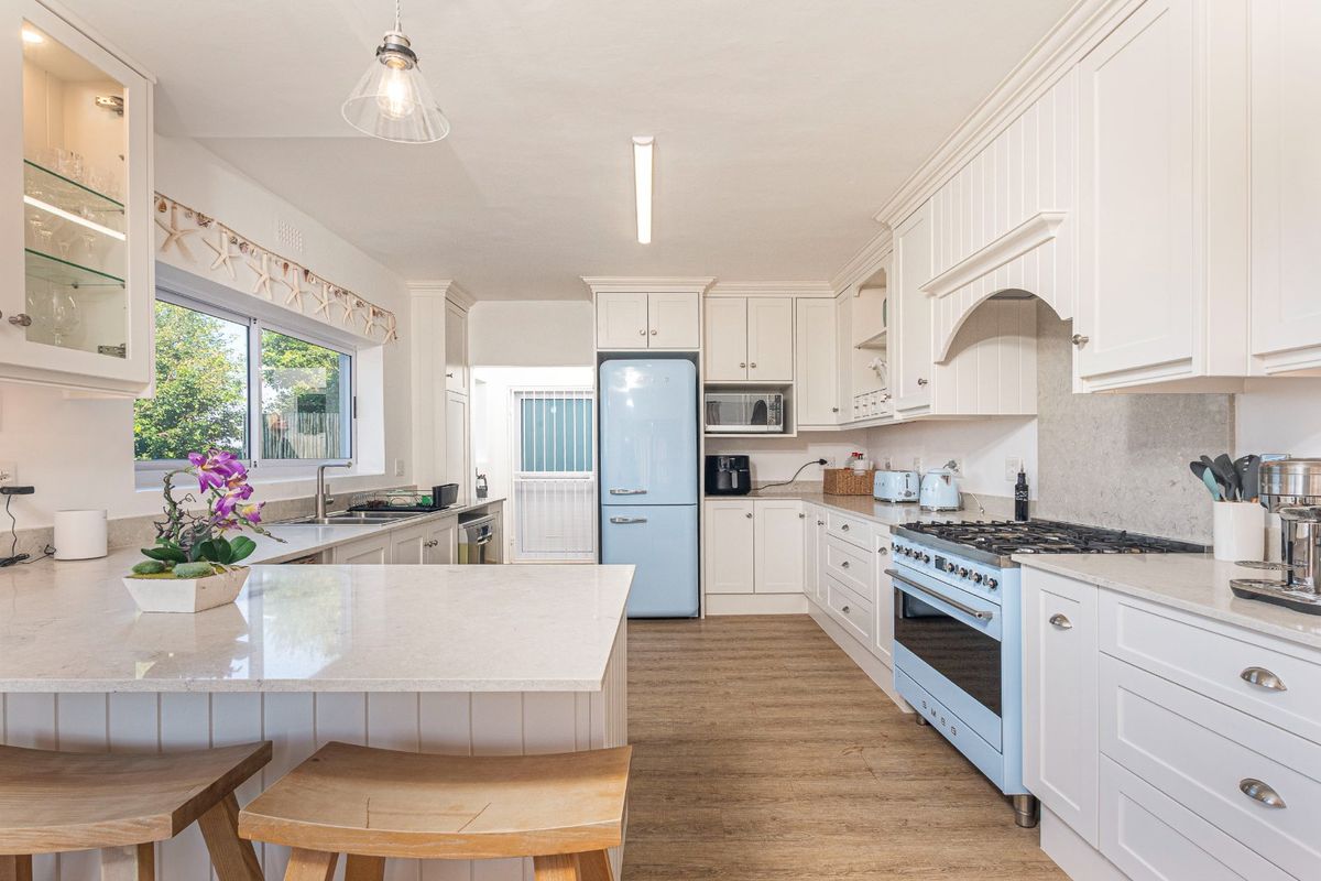 A bright, well-maintained kitchen featuring white shaker-style cabinetry, quartz countertops, a gas range, and a breakfast bar island with wood-look flooring.