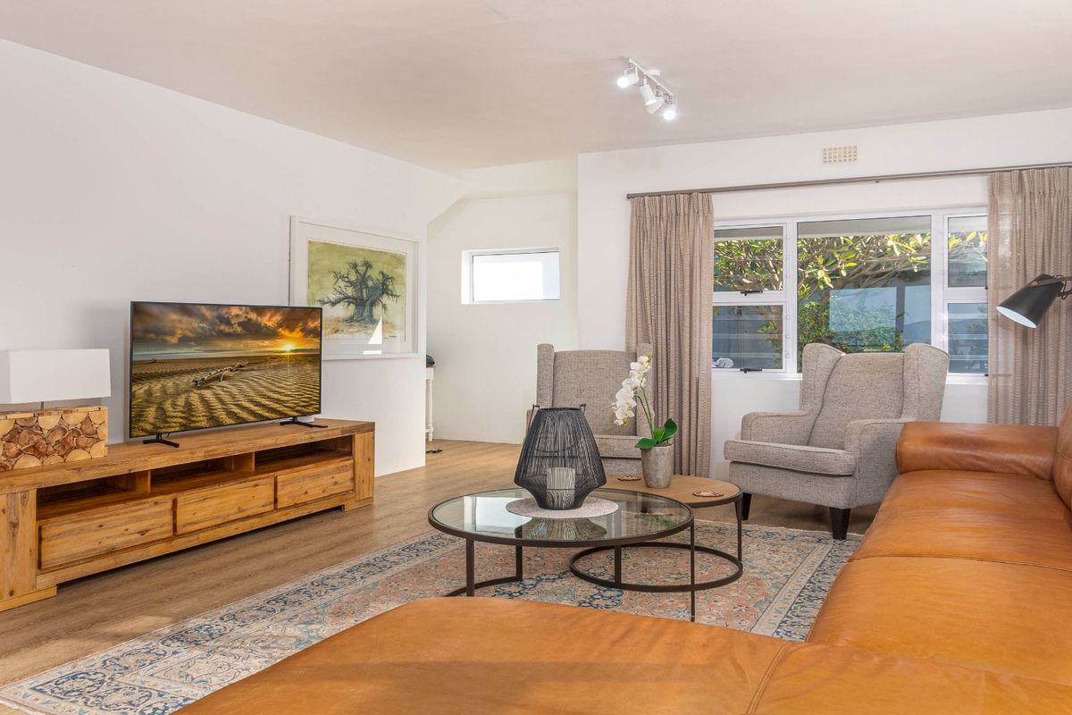 A bright and well-maintained living room featuring laminate flooring, modern track lighting, and large windows that provide ample natural light.