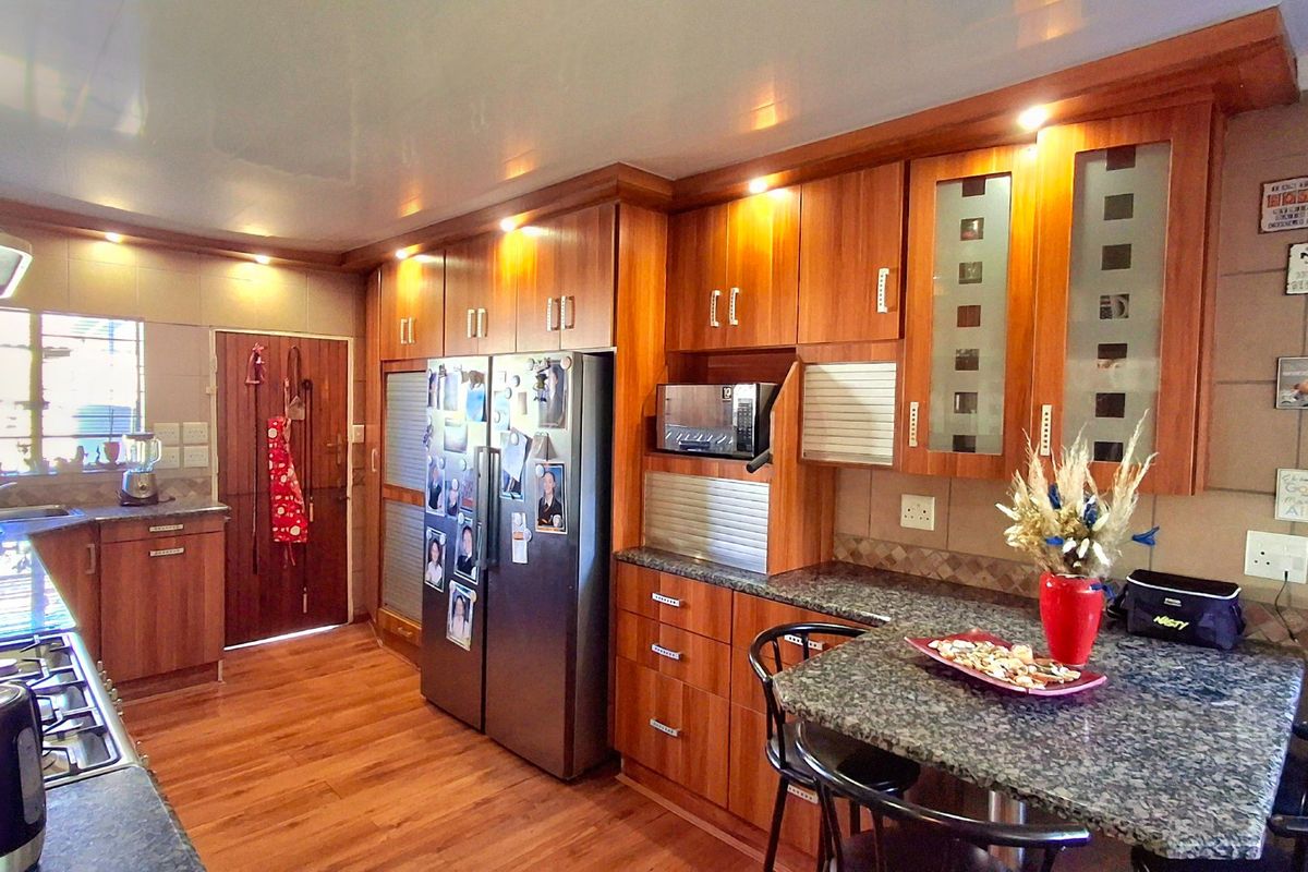 A functional kitchen featuring warm-toned wooden cabinetry, granite countertops, integrated appliances, and laminate flooring, offering a practical layout for daily meal preparation.