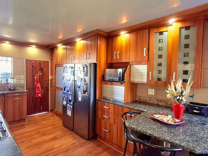 A functional kitchen featuring warm-toned wooden cabinetry, granite countertops, integrated appliances, and laminate flooring, offering a practical layout for daily meal preparation.