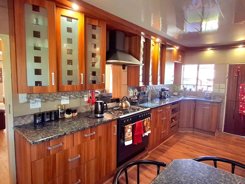 A functional kitchen featuring warm-toned wooden cabinetry, granite countertops, a gas stove with extractor fan, and durable laminate flooring.