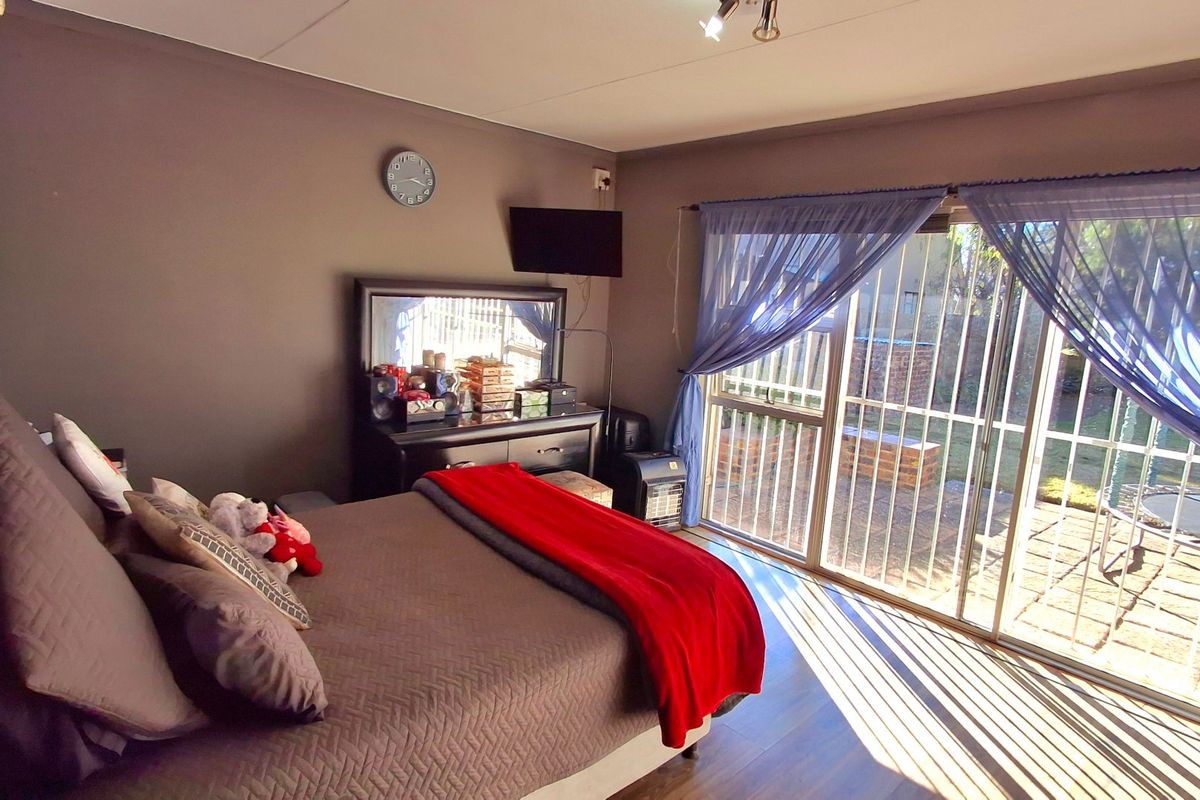 A bedroom featuring laminate flooring and a large sliding glass door with an integrated security gate, providing direct access to the outdoor area.