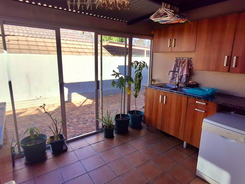 A functional scullery or utility area featuring built-in wooden cabinetry, a double sink, and direct access to the outdoor patio through sliding glass doors.