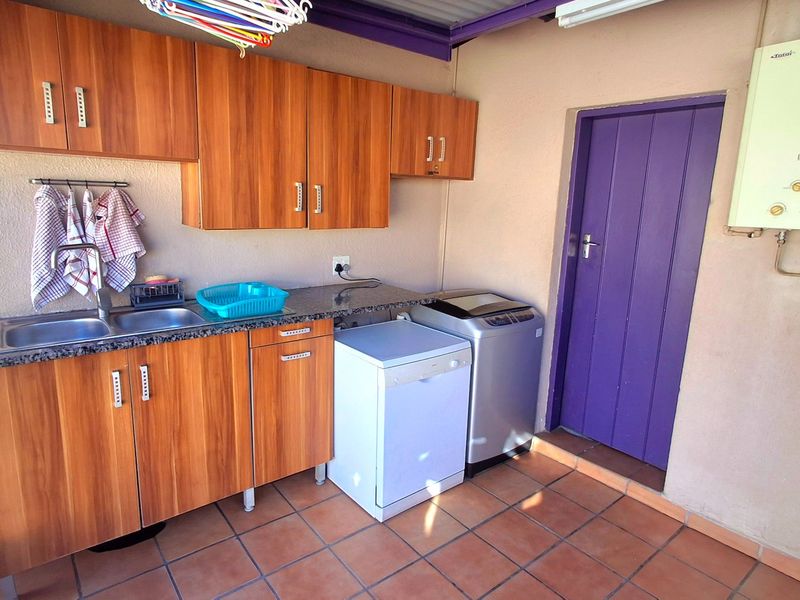 Functional laundry area featuring built-in wooden cabinetry, granite countertops, a stainless steel sink, and a wall-mounted gas geyser.