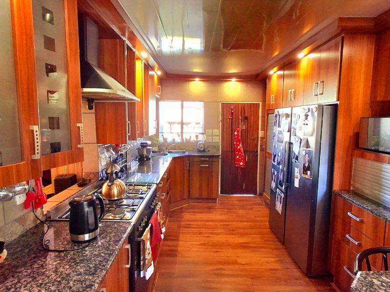 A functional kitchen featuring extensive wooden cabinetry, granite countertops, a gas hob with extractor, and integrated appliances, with some visible ceiling panel wear.