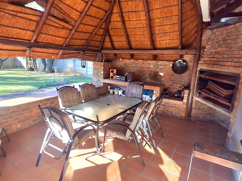 Covered outdoor patio featuring a traditional thatched roof, exposed brickwork, and a built-in braai area, overlooking the garden.