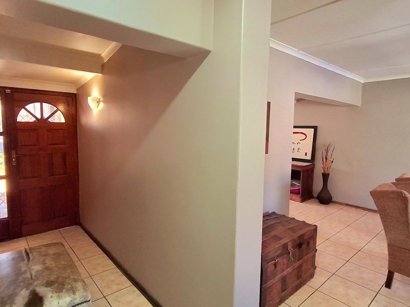 A welcoming entrance hall featuring ceramic floor tiles, a solid timber front door with glass detailing, and warm wall sconce lighting.
