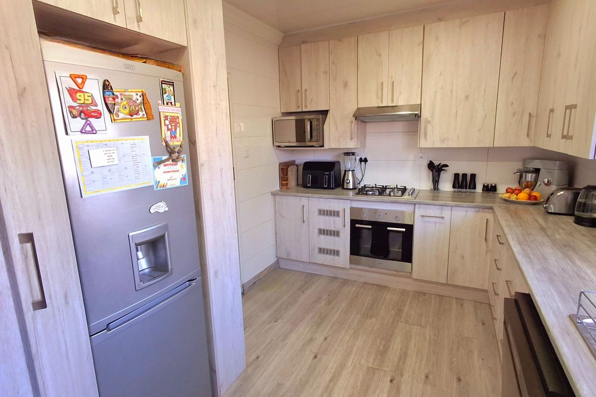 A well-maintained kitchen featuring light wood-grain cabinetry, laminate countertops, and integrated appliances including a gas hob, oven, and extractor fan.