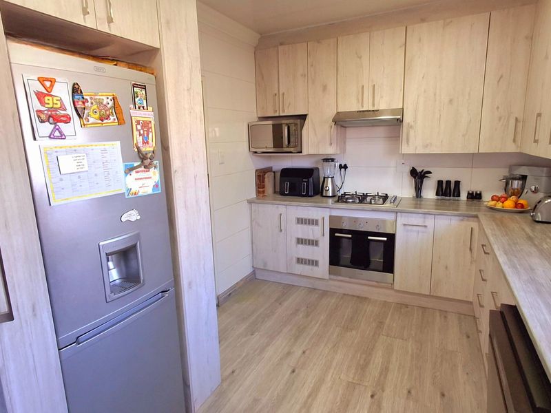 A well-maintained kitchen featuring light wood-grain cabinetry, laminate countertops, and integrated appliances including a gas hob, oven, and extractor fan.