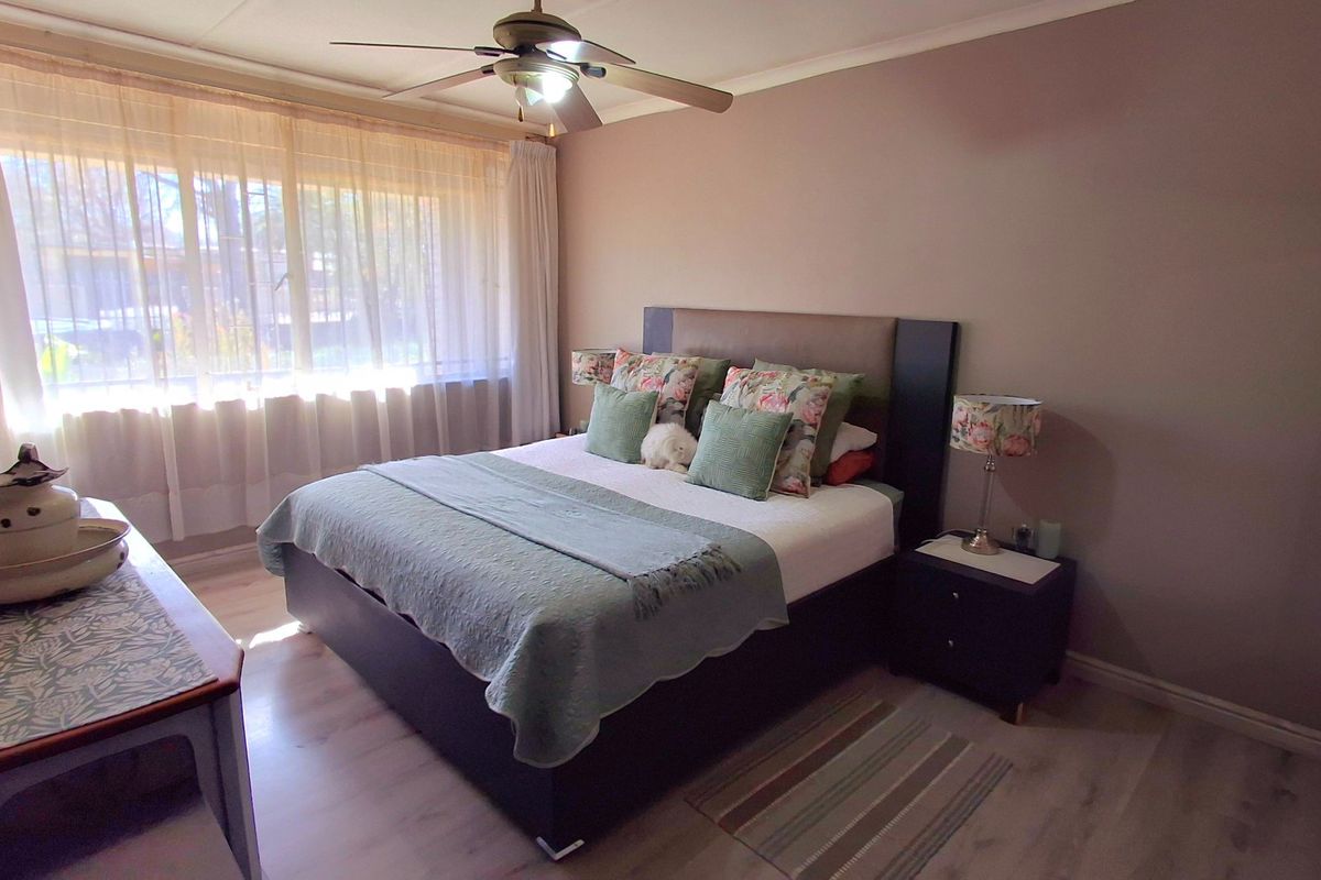 A well-maintained bedroom featuring laminate flooring, a ceiling fan, and large windows with curtain tracks, providing a comfortable and functional living space.