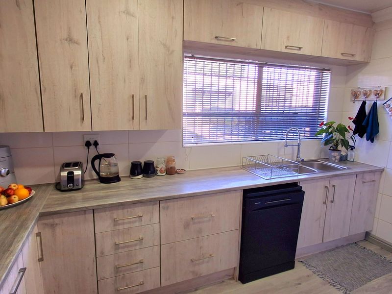 A functional kitchen featuring light wood-look cabinetry, laminate countertops, a stainless steel sink, and a tiled backsplash with integrated dishwasher.