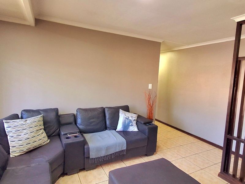 A living room featuring neutral wall tones, tiled flooring, and a decorative timber room divider, providing a functional and open living space.