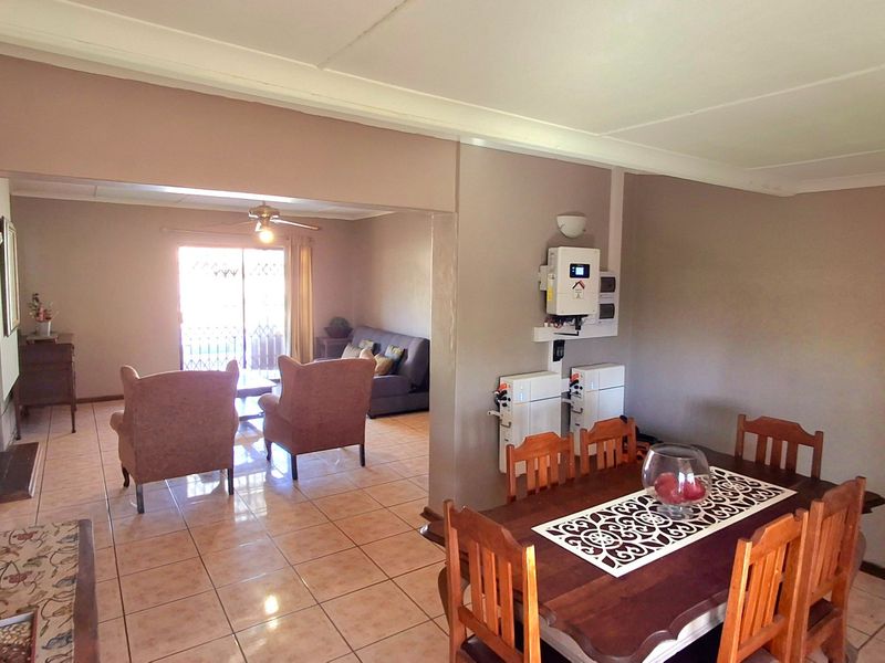 Open-plan living and dining area featuring tiled flooring, a ceiling fan, and a wall-mounted solar inverter and battery storage system.