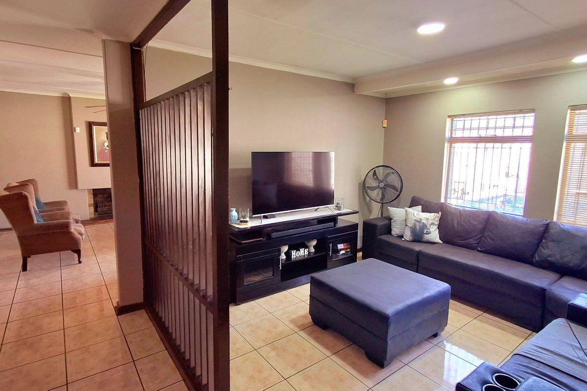A living room featuring tiled flooring, recessed ceiling lighting, and a decorative room divider, with security bars installed on the windows.