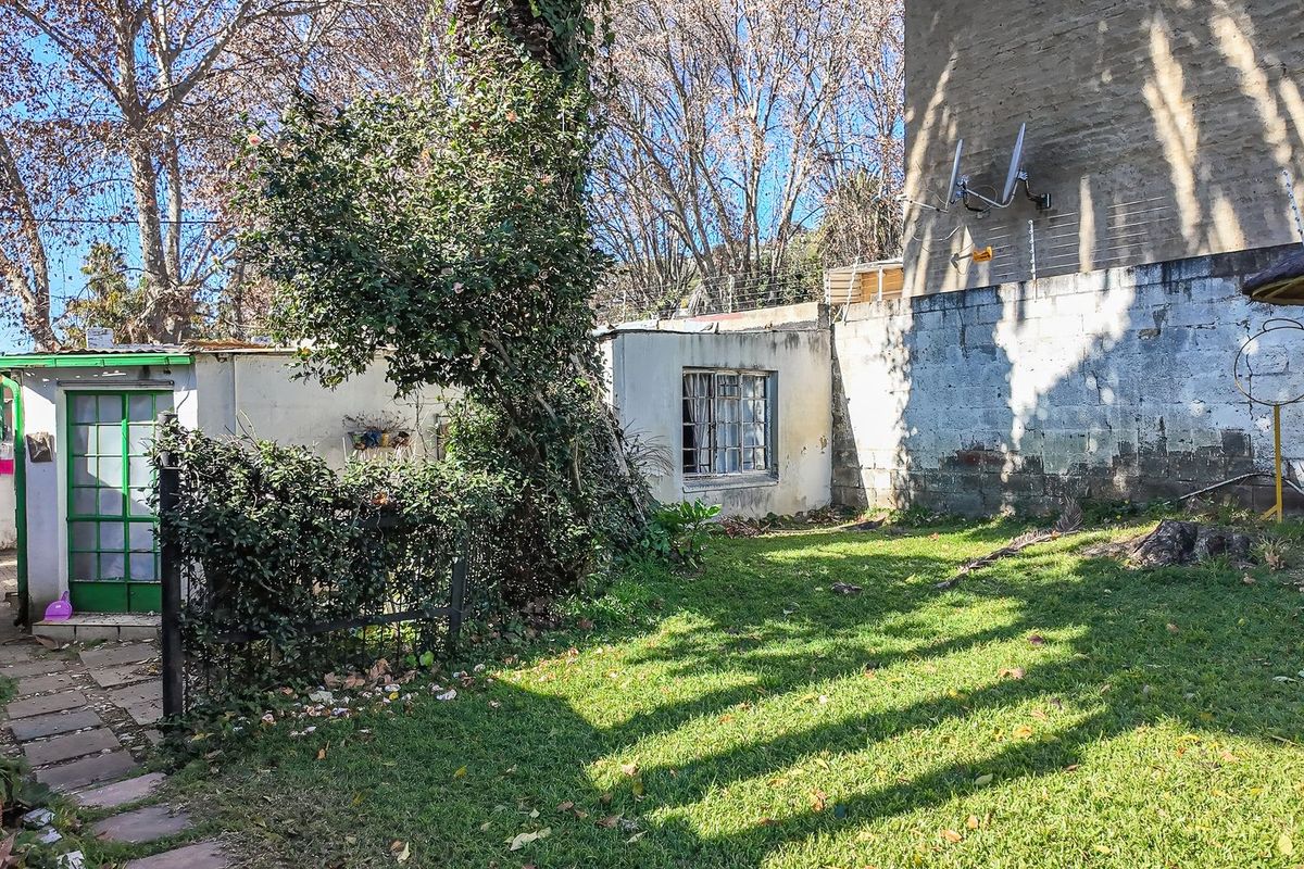 Rear garden area featuring a lawn, paved walkway, and concrete block boundary walls with electric fencing and visible signs of weathering.
