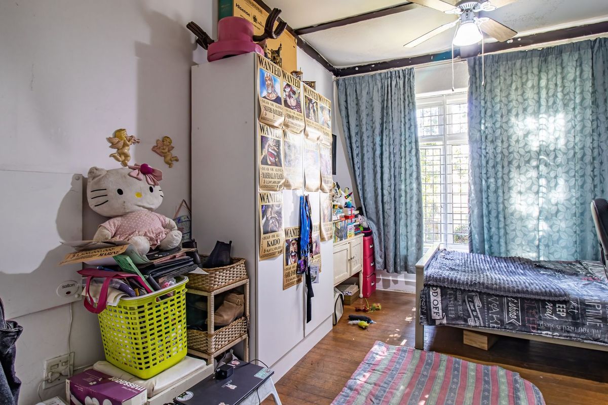 A bedroom featuring timber flooring, a ceiling fan, and security bars on the window, currently showing signs of wear and dated finishes.