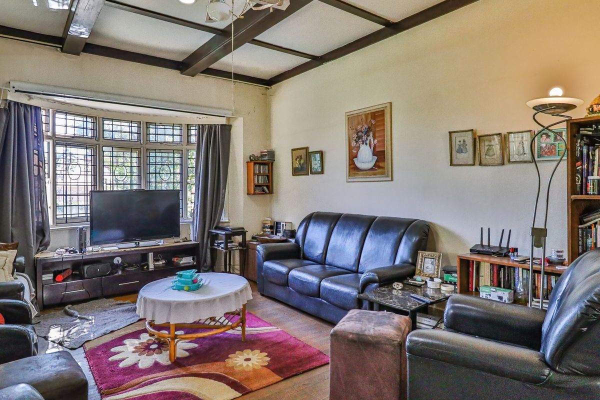 A living room featuring exposed timber ceiling beams, a large leaded glass bay window, and hardwood flooring, offering a traditional character space.