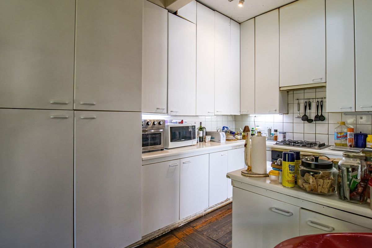 A functional kitchen featuring white cabinetry, a gas hob, built-in oven, and tiled backsplash, with potential for cosmetic updates to the flooring and cabinetry.
