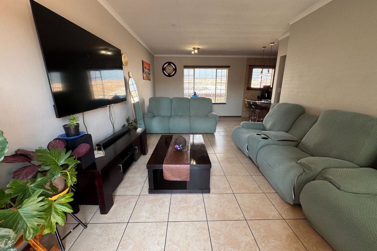 Open plan living area featuring ceramic floor tiles, neutral wall finishes, and a breakfast bar leading into the kitchen space.